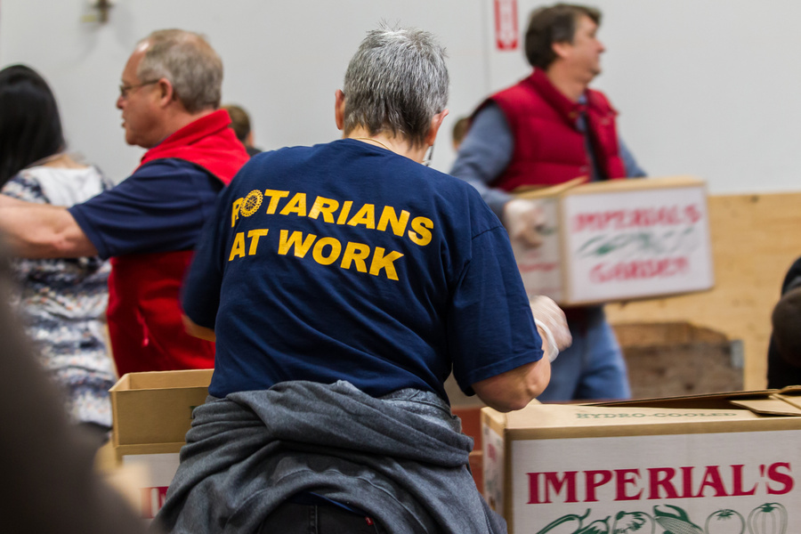 a group of Rotary members in a warehouse with boxes of food